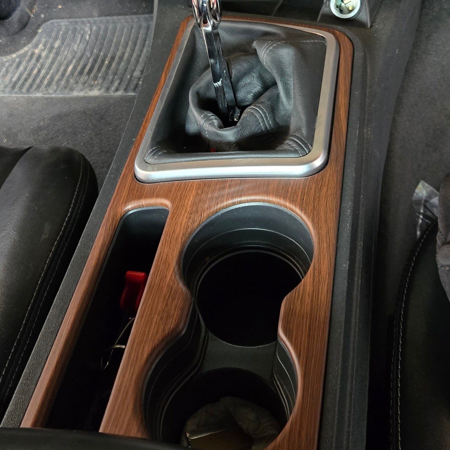 Car interior dashboard with wooden panel, gear shift, and cup holders.